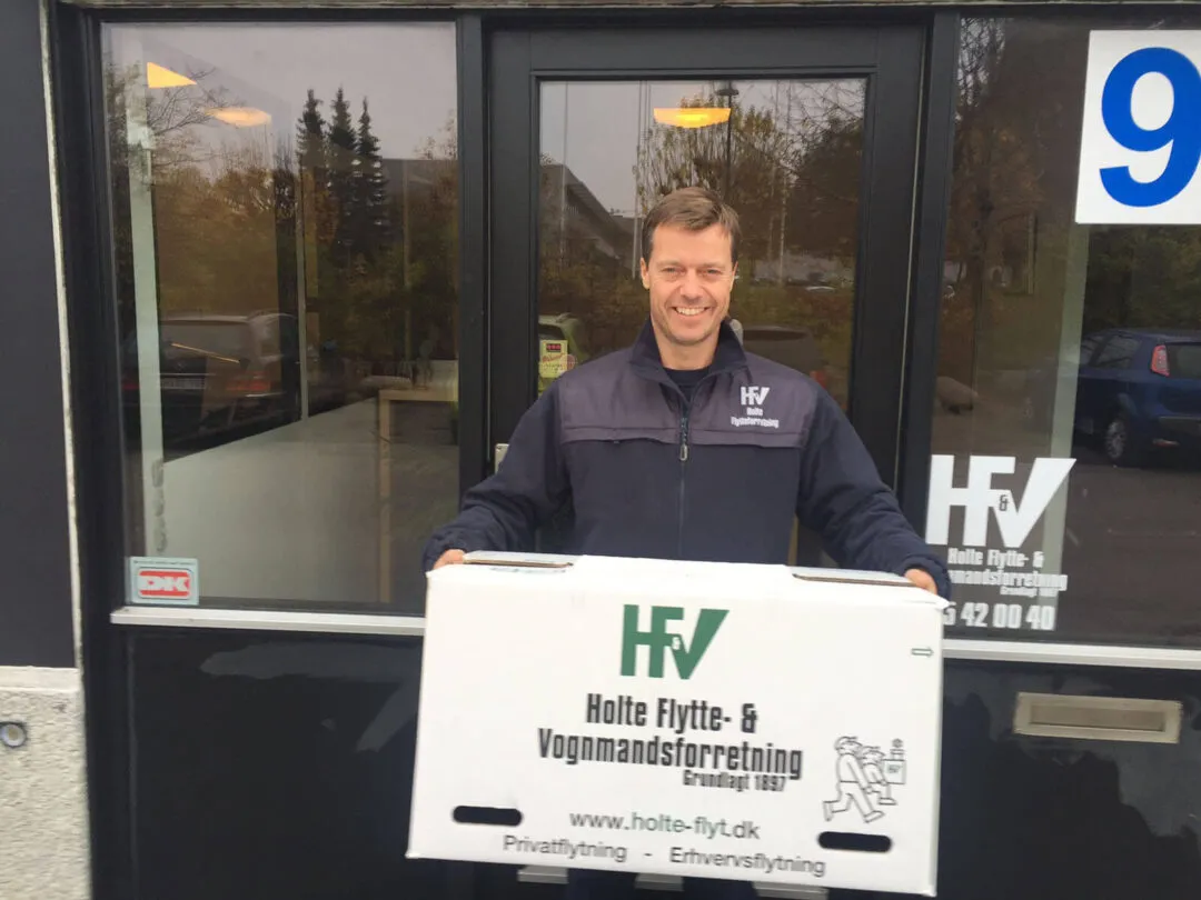 Medarbejder fra Holte Flytte med en HF&V flyttekasse foran kontoret i Birkerød